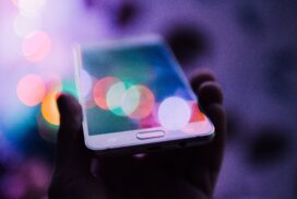 A silhouetted hand holding a mobile smart phone with colorful abstract lights surrounding it