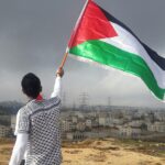 Person waving a Palestinian flag, photo by Ahmed Abu Hameeda